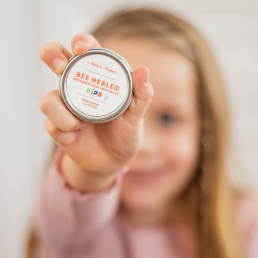 Child holding a 'Bee Healed Kids' product tin against a blurred background