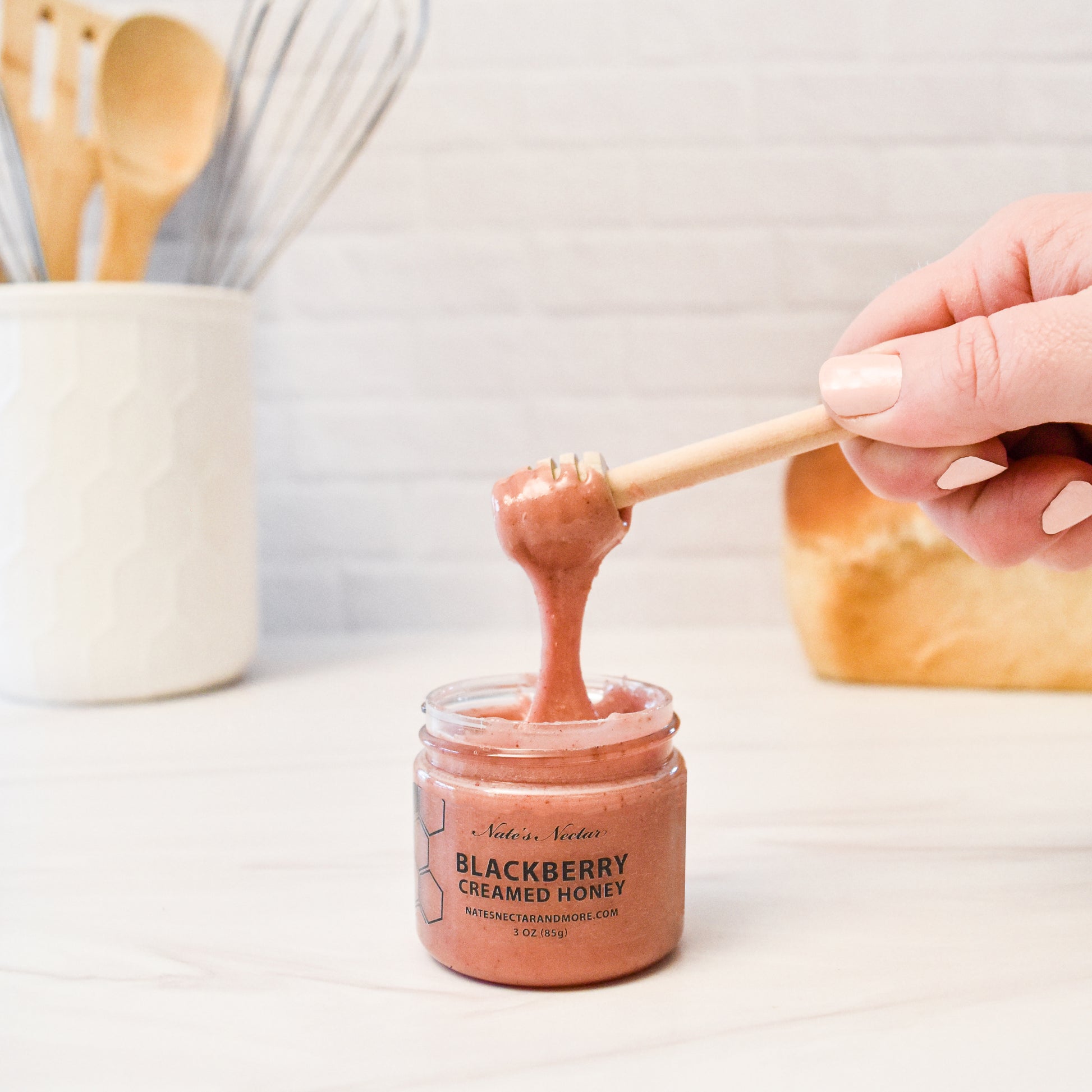 person using wooden spoon to get blackberry creamed honey out of jar