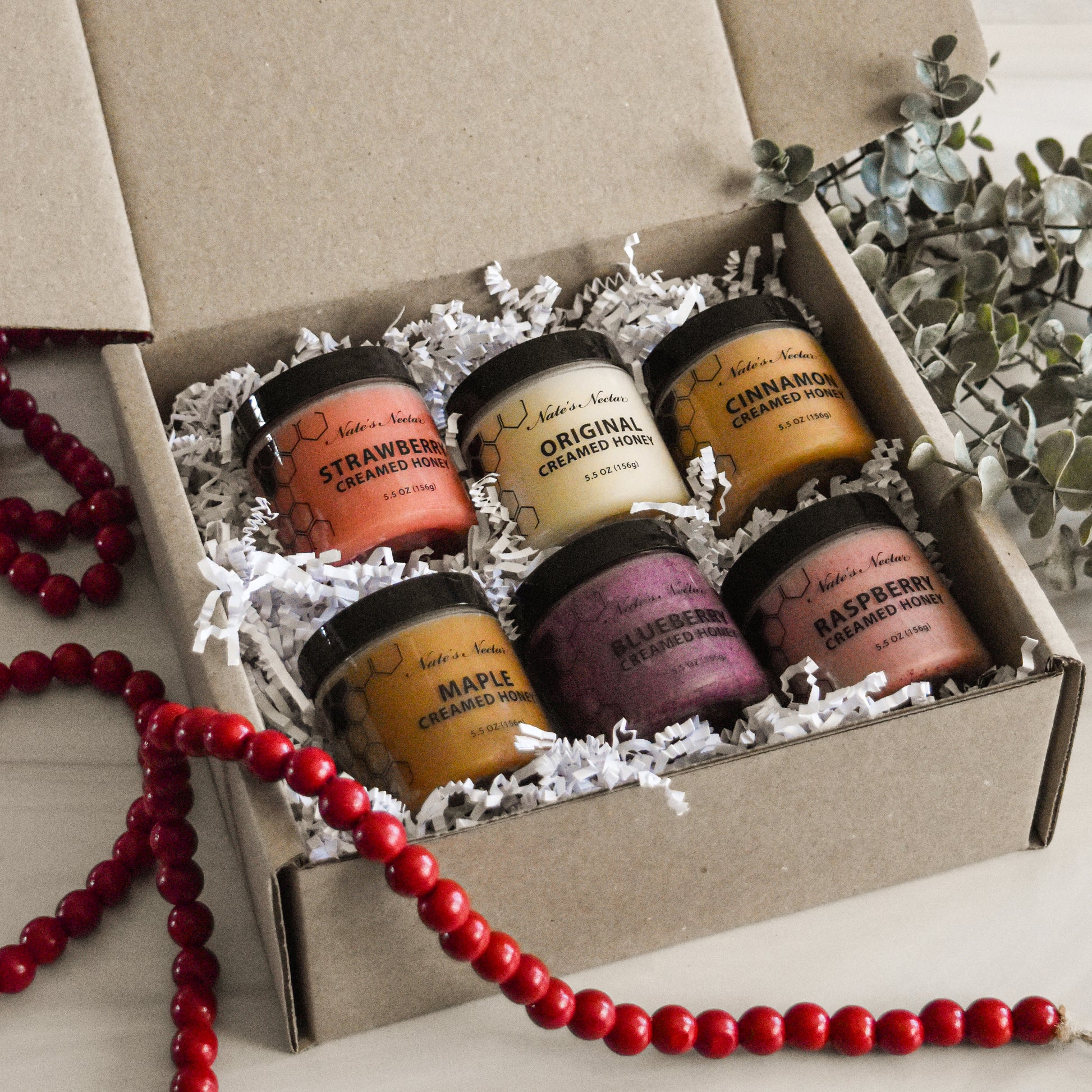 Set of six small jars with labels in a box, surrounded by decorative elements.