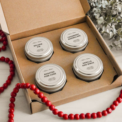 Four metal tins with labels in a cardboard box, surrounded by red beads and greenery.