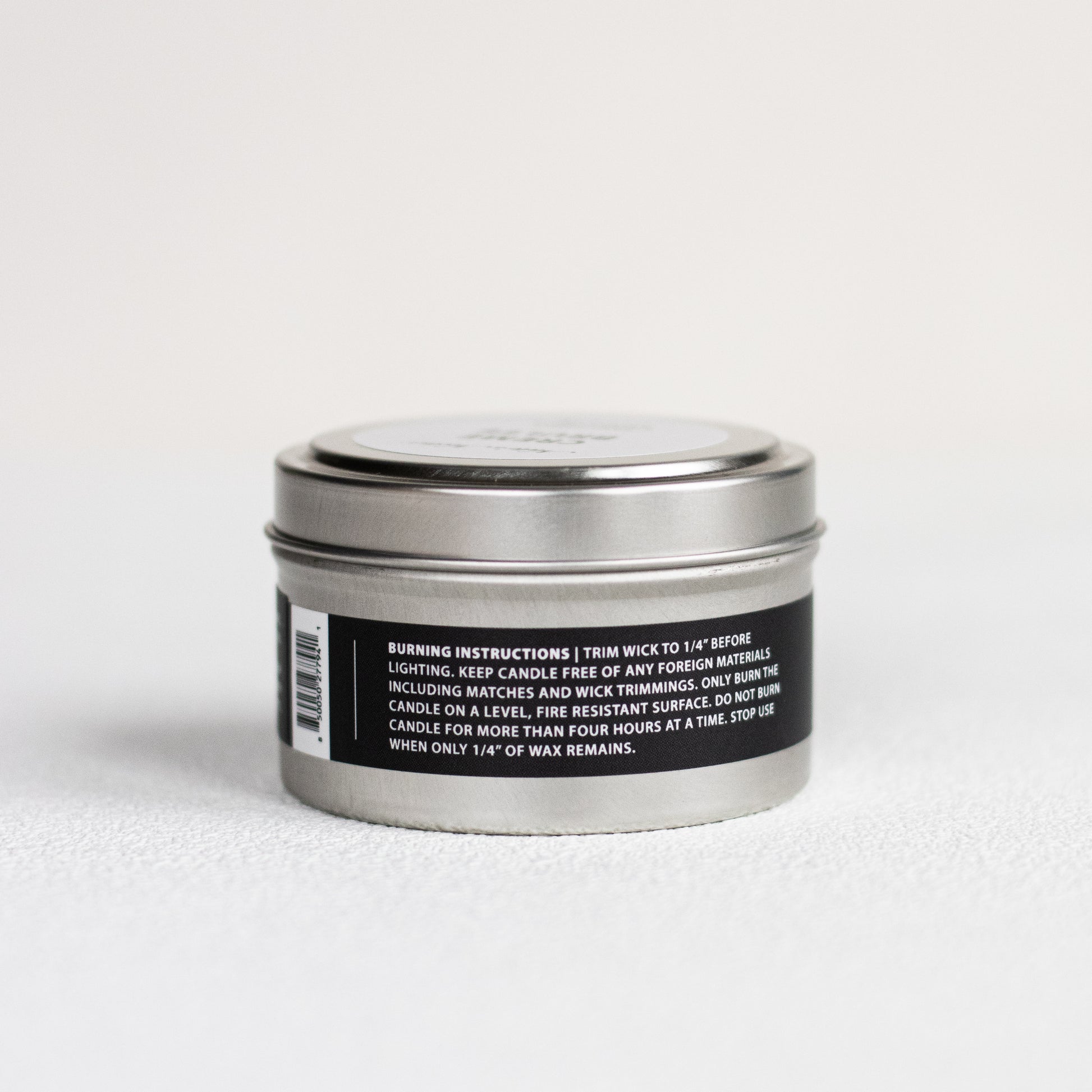 Silver candle tin with a black label on a white background