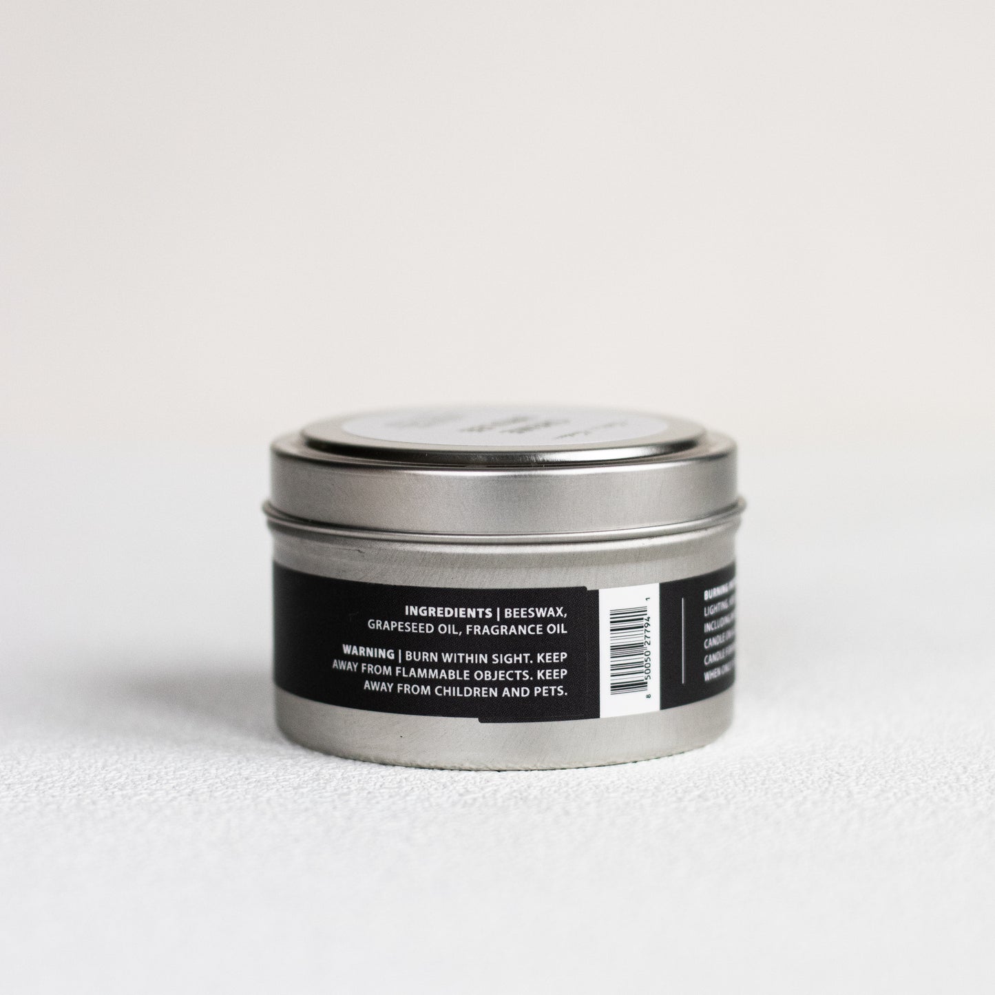 Silver candle tin with a black label on a light gray background