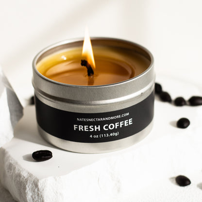Candle in a tin labeled 'Fresh Coffee' with coffee beans around on a light background