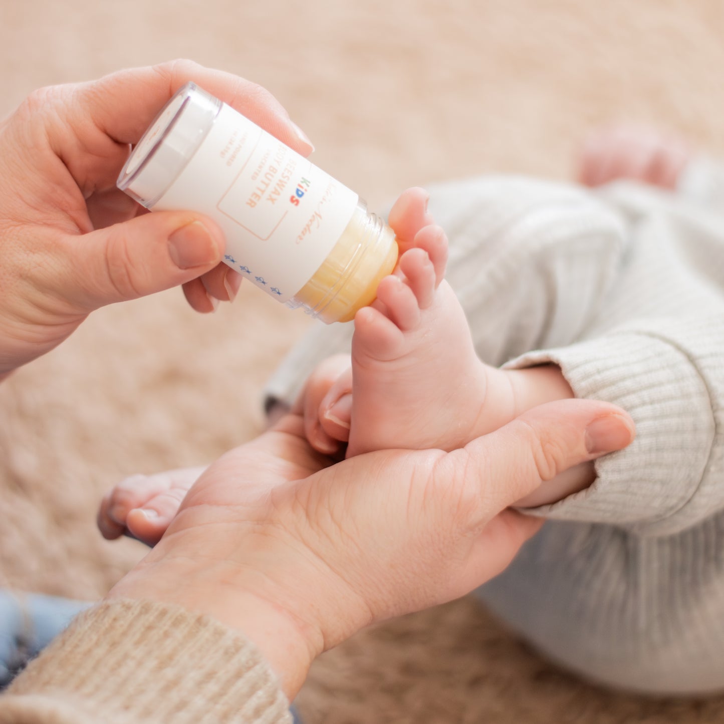 person holding baby's foot while applying kids beeswax body butter
