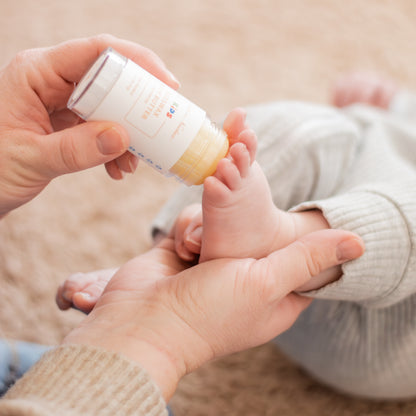 person holding baby's foot while applying kids beeswax body butter