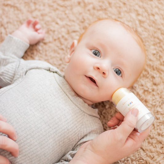 Baby lying on a carpeted floor with a Kids Body Butter being applied to his cheek