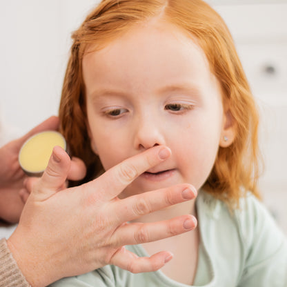 Child with red hair being shown a small container by an adult hand.