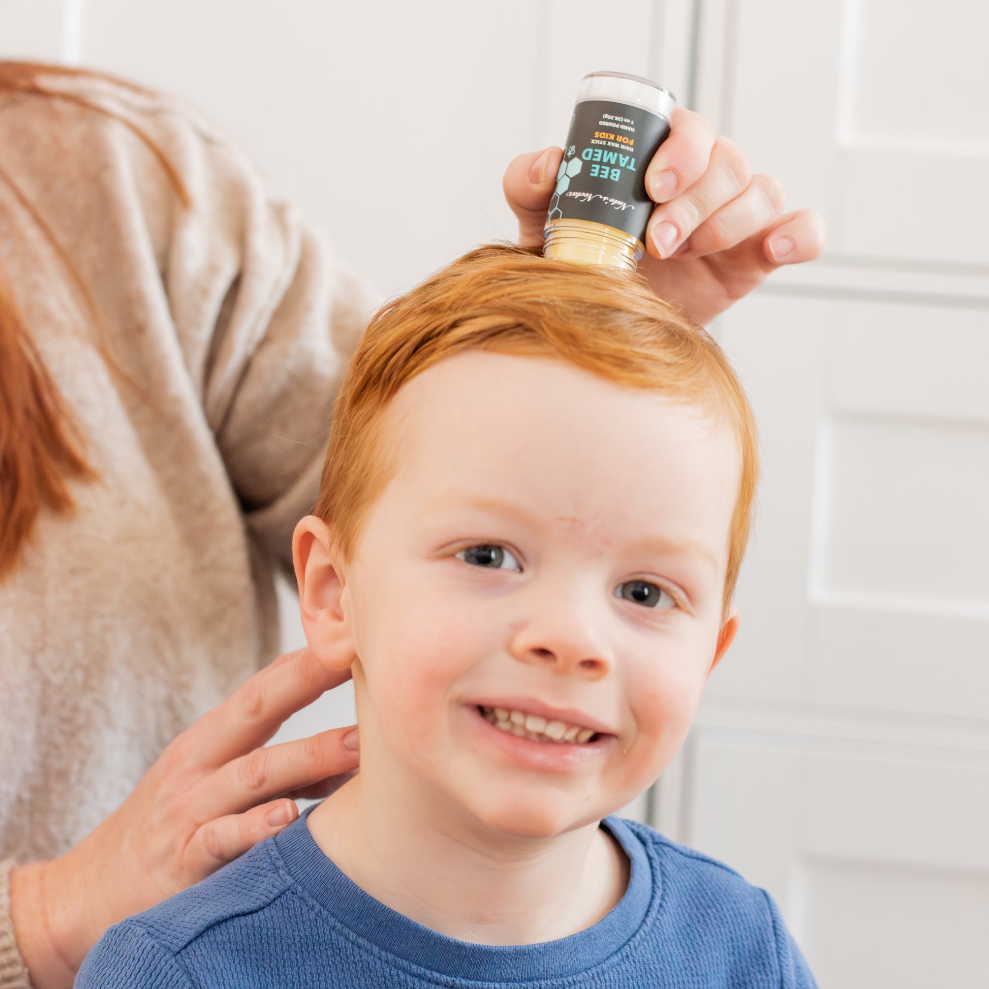 Child with red hair being combed by a person, with a product container held above.