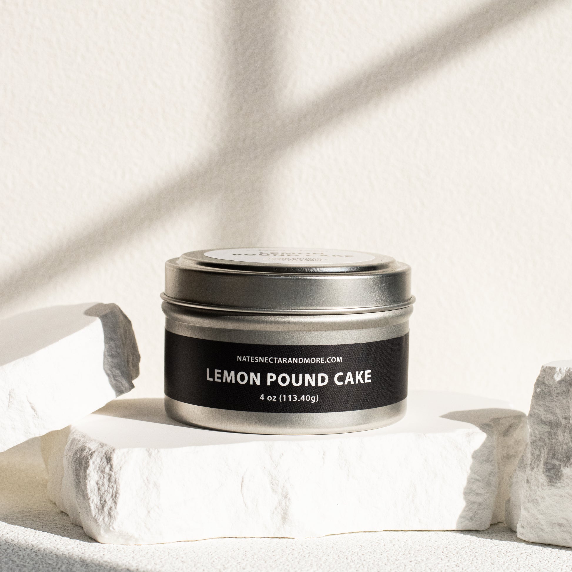 Candle tin labeled 'Lemon Pound Cake' on a light fabric background