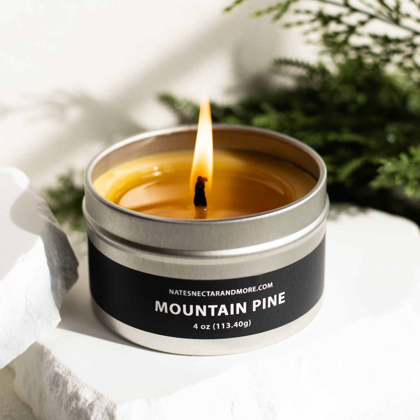 Candle in a metal tin labeled 'Mountain Pine' with a blurred natural background