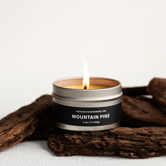 Candle in a metal tin labeled 'Mountain Pine' on a white background with wooden elements.