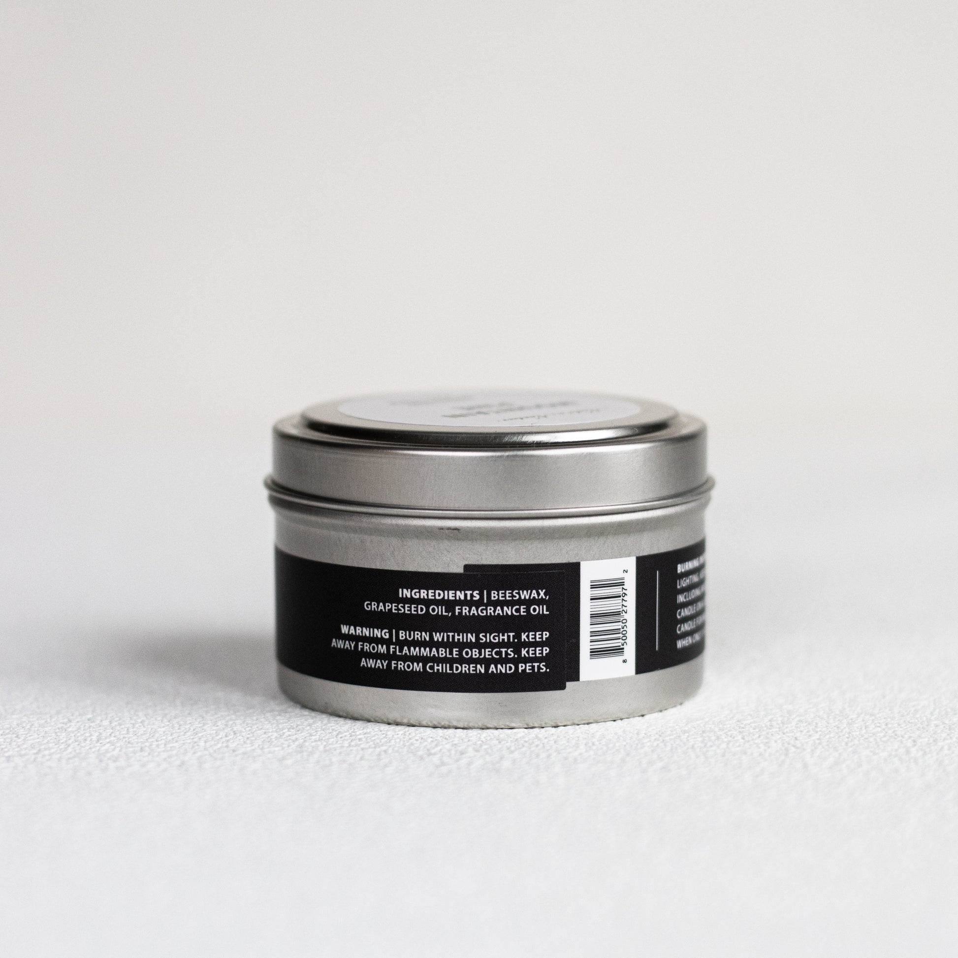 Silver candle tin with a black label on a light gray background