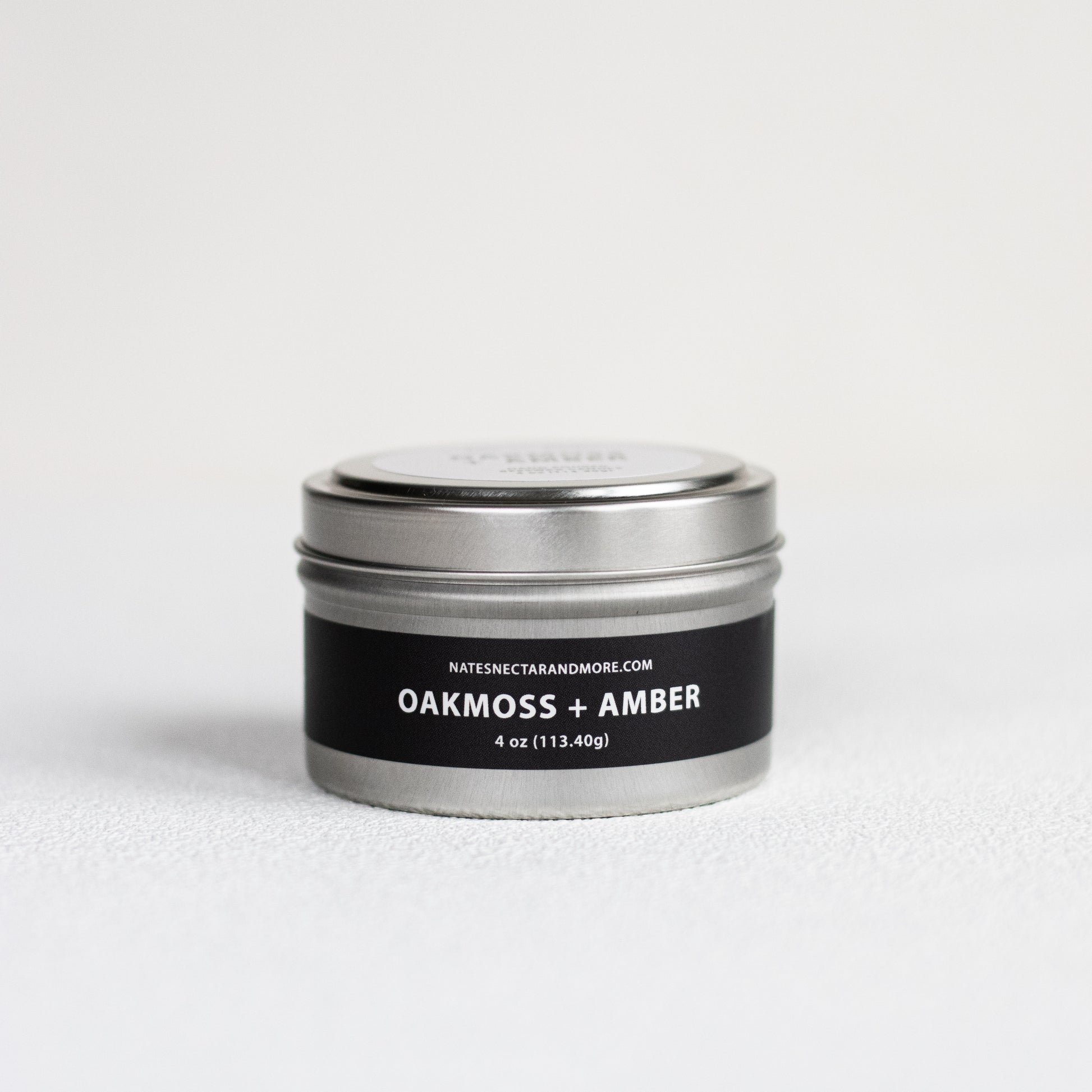 Candle tin labeled 'Oakmoss + Amber' on a white background