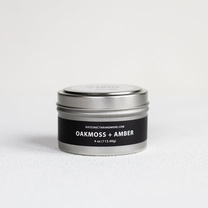 Candle tin labeled 'Oakmoss + Amber' on a white background