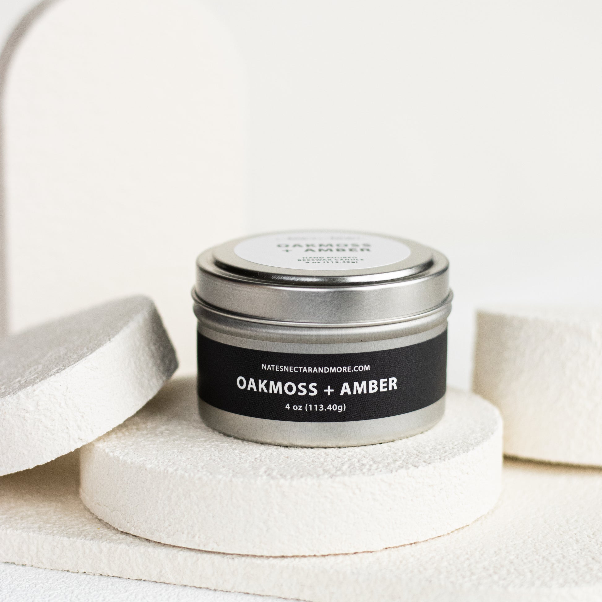 Candle tin labeled 'Oakmoss + Amber' on a white background