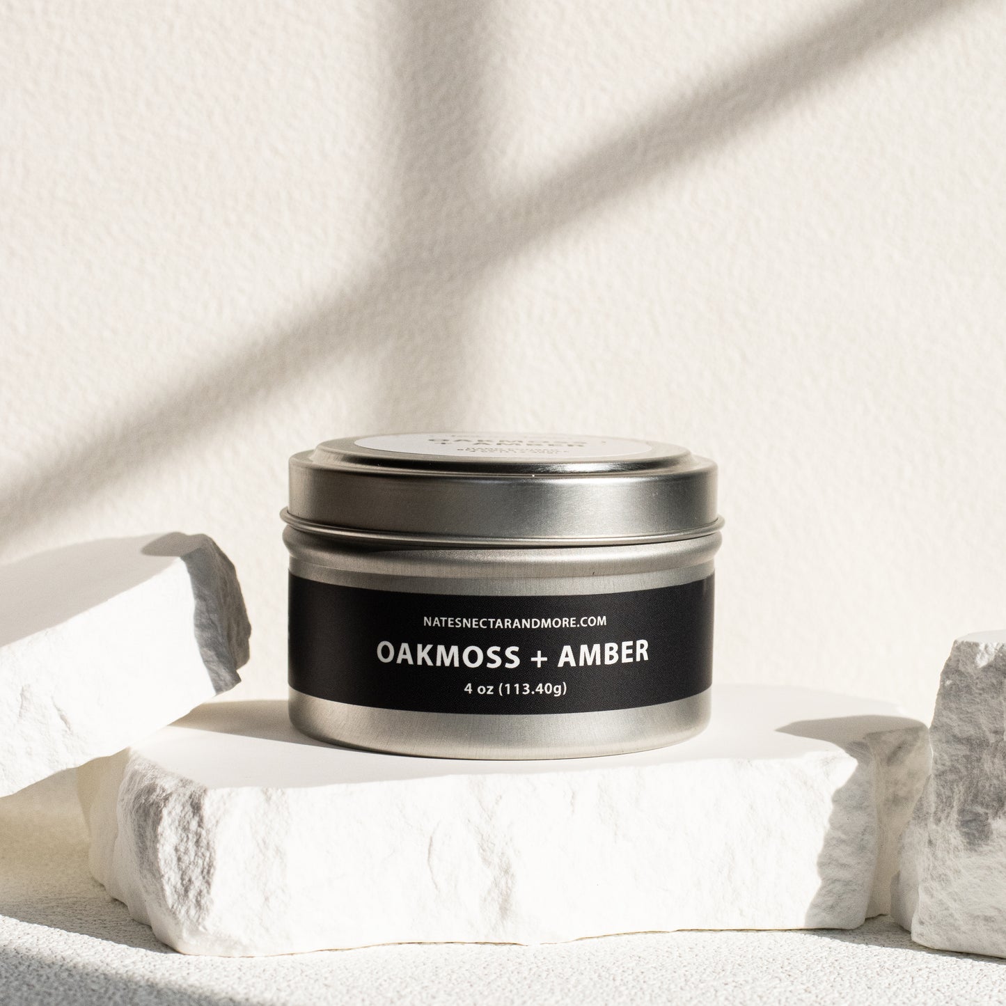 Silver tin labeled 'Oakmoss + Amber' on a light background