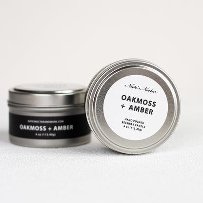 Two tins of 'Oakmoss + Amber' candles by Nade's Nook on a white background