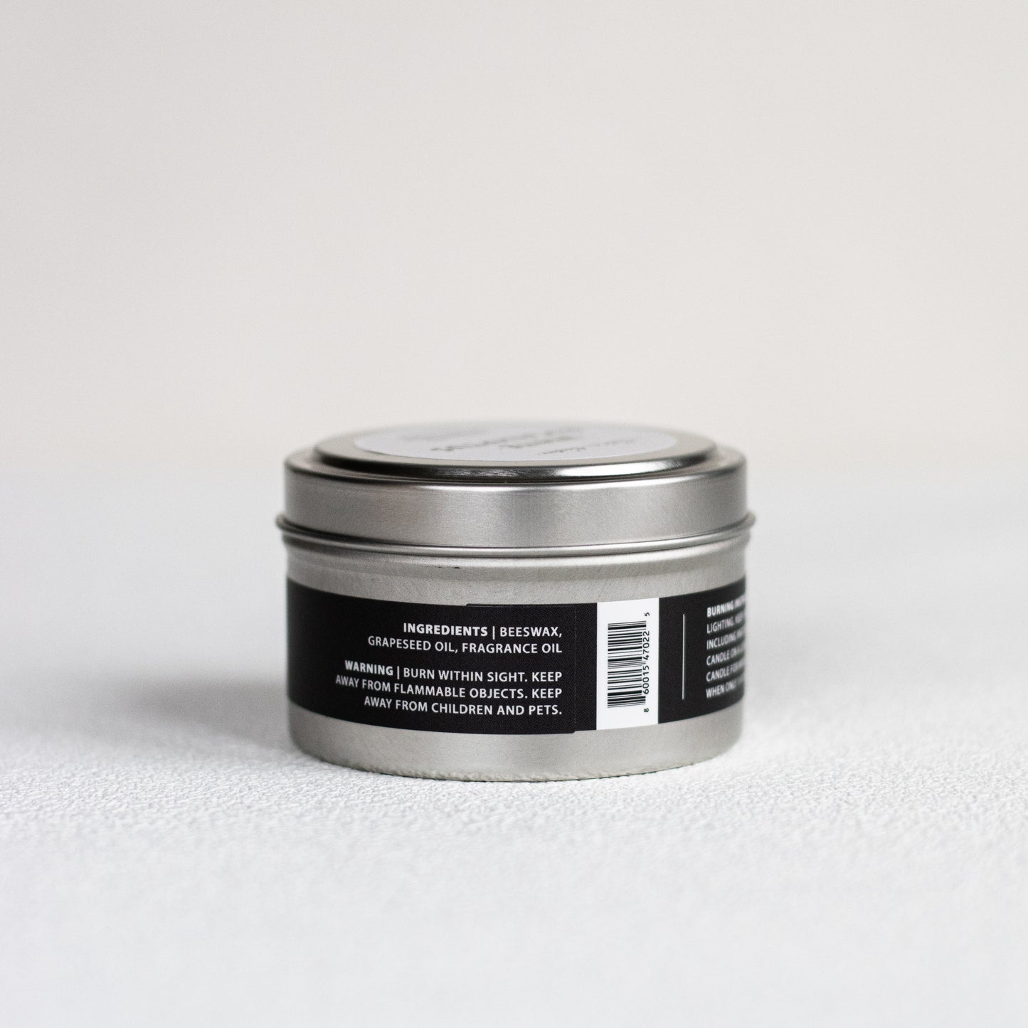 Silver candle tin with black label on a light gray background
