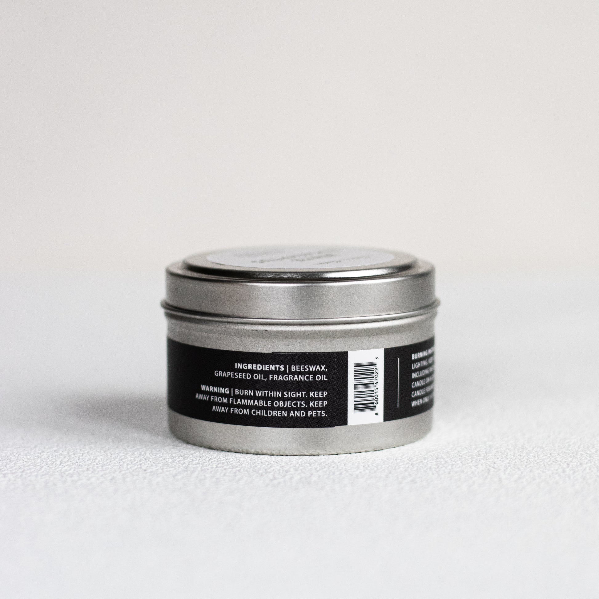Silver candle tin with black label on a light gray background